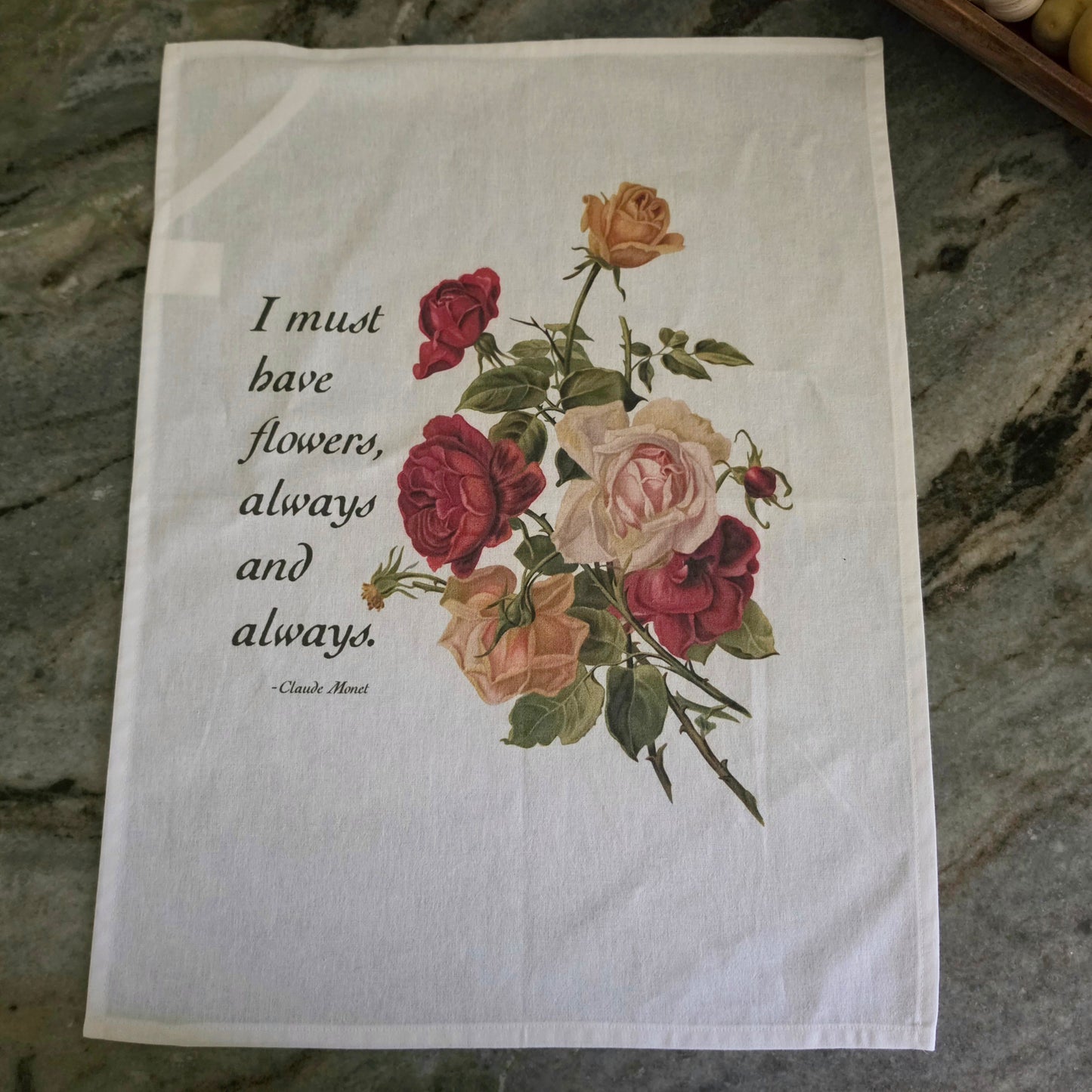 A square white tea towel featuring a vintage-style floral bouquet of red, pink, and yellow roses with green leaves, alongside the quote 'I must have flowers, always and always.' by Claude Monet.