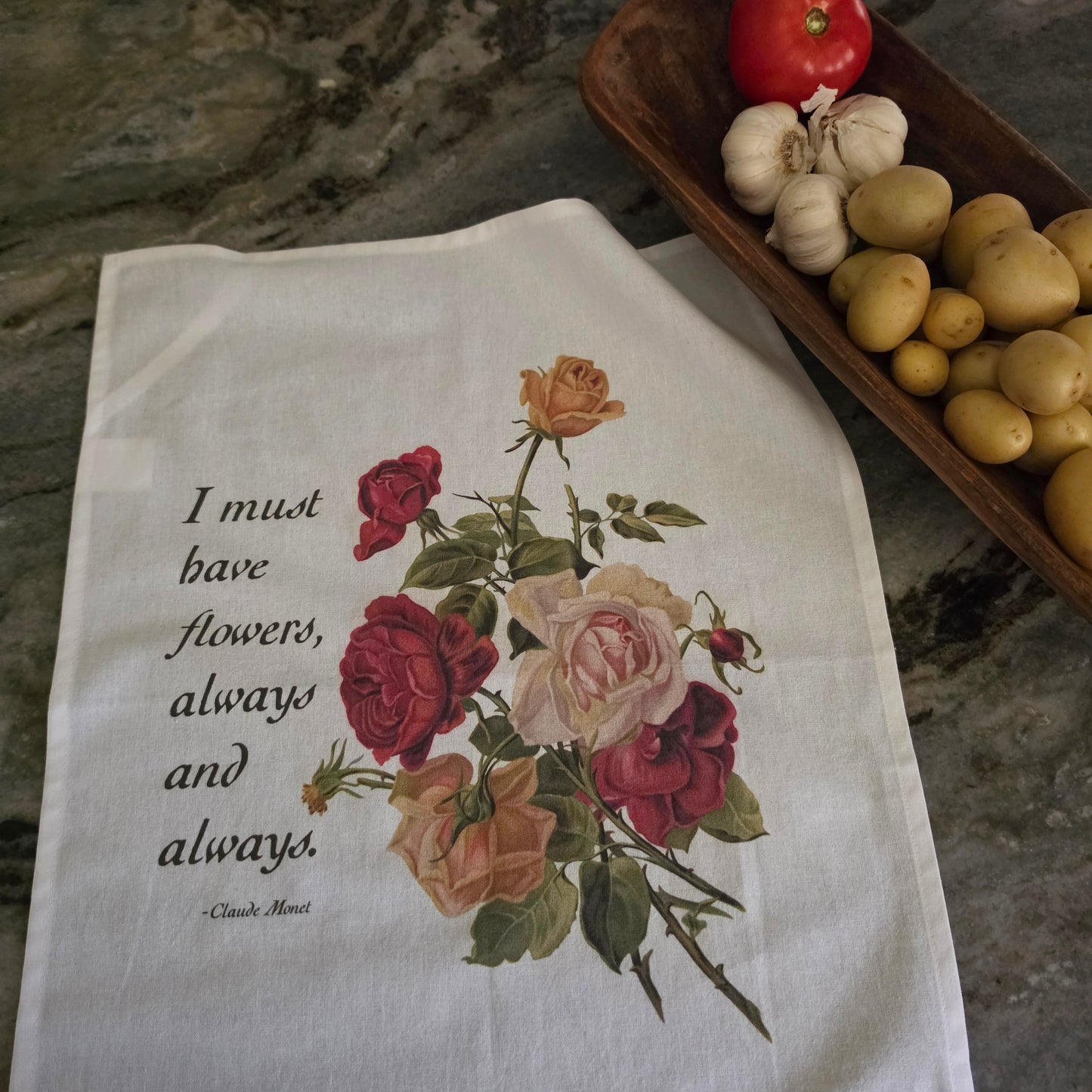 A white kitchen tea towel featuring a vintage-style floral print of red, pink, and peach roses with green leaves, alongside the quote 'I must have flowers, always and always.' from Claude Monet.