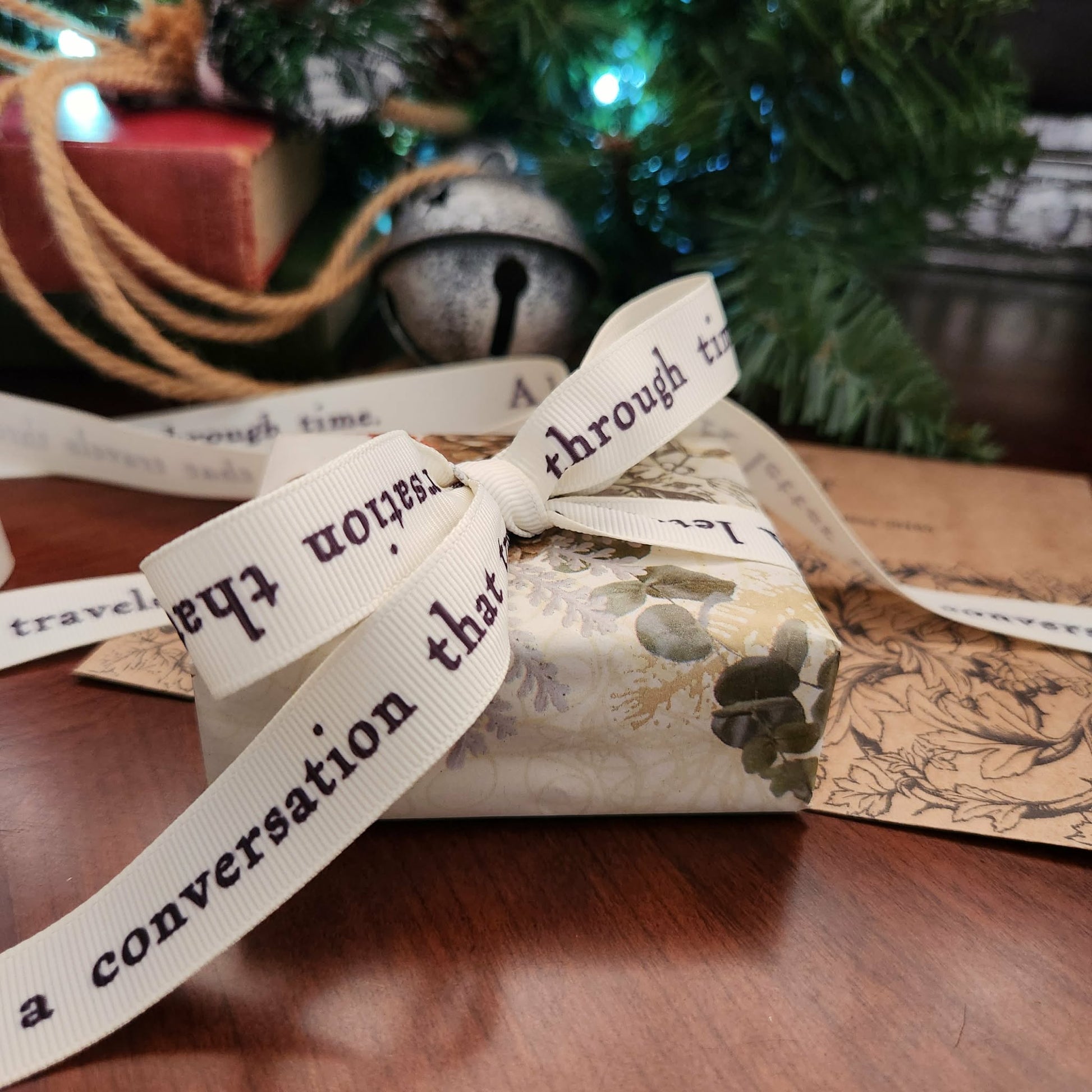 Gift wrapped in floral paper with a decorative ribbon in front of a Christmas tree.