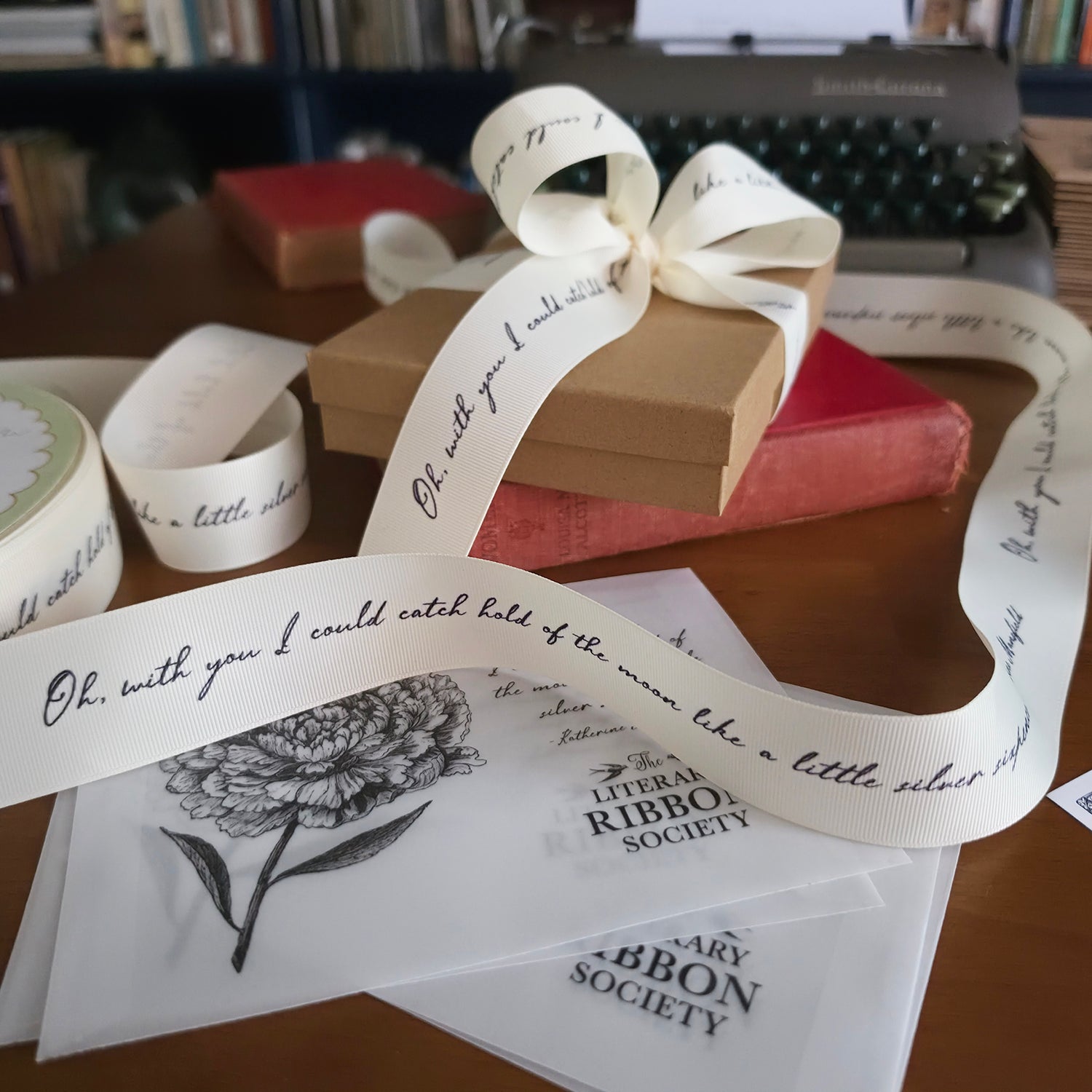 Decorative ribbon with text and floral design on a surface with books and a typewriter in the background.