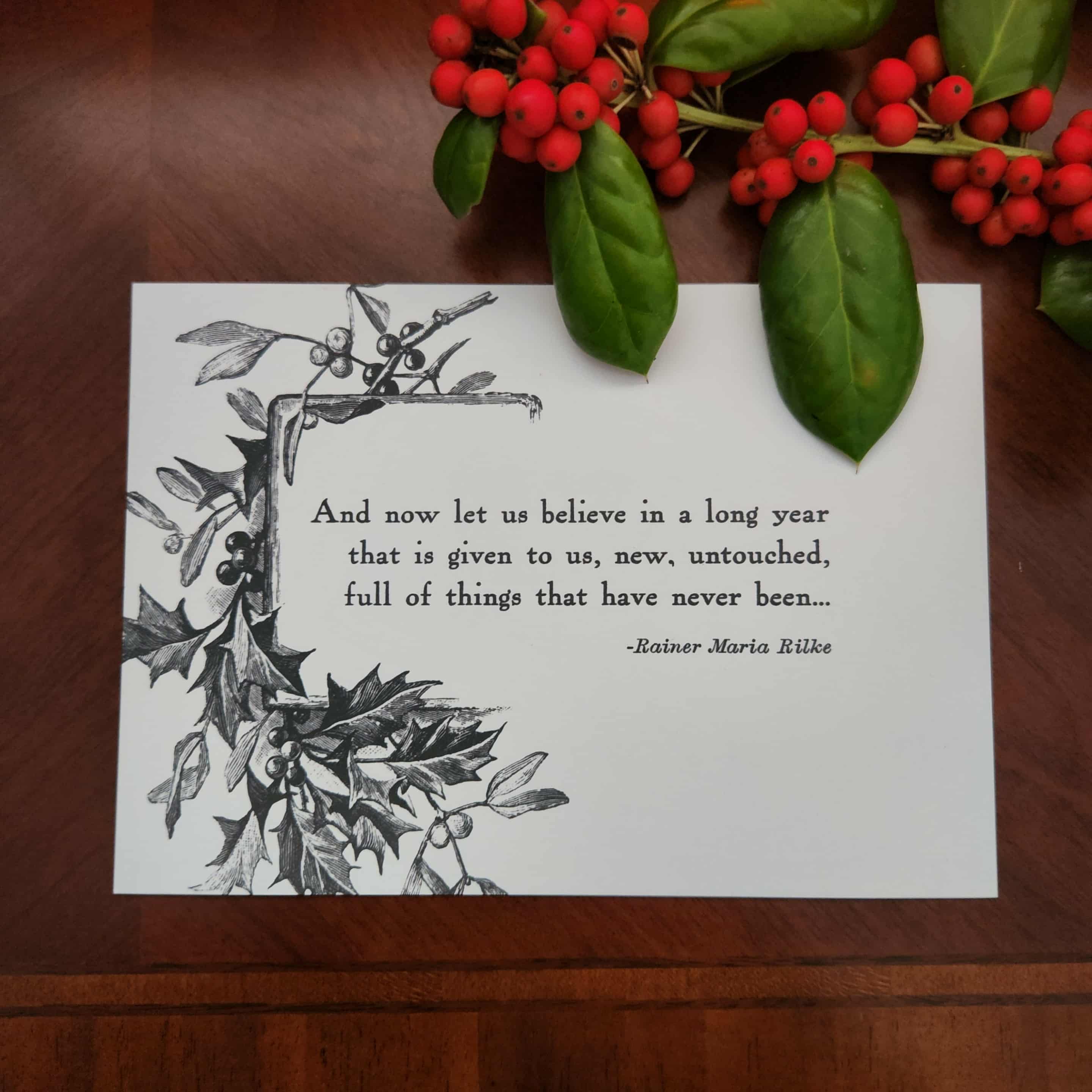 Art print from The Prose & Post Society with holly design and quote on a wooden surface with holly berries.