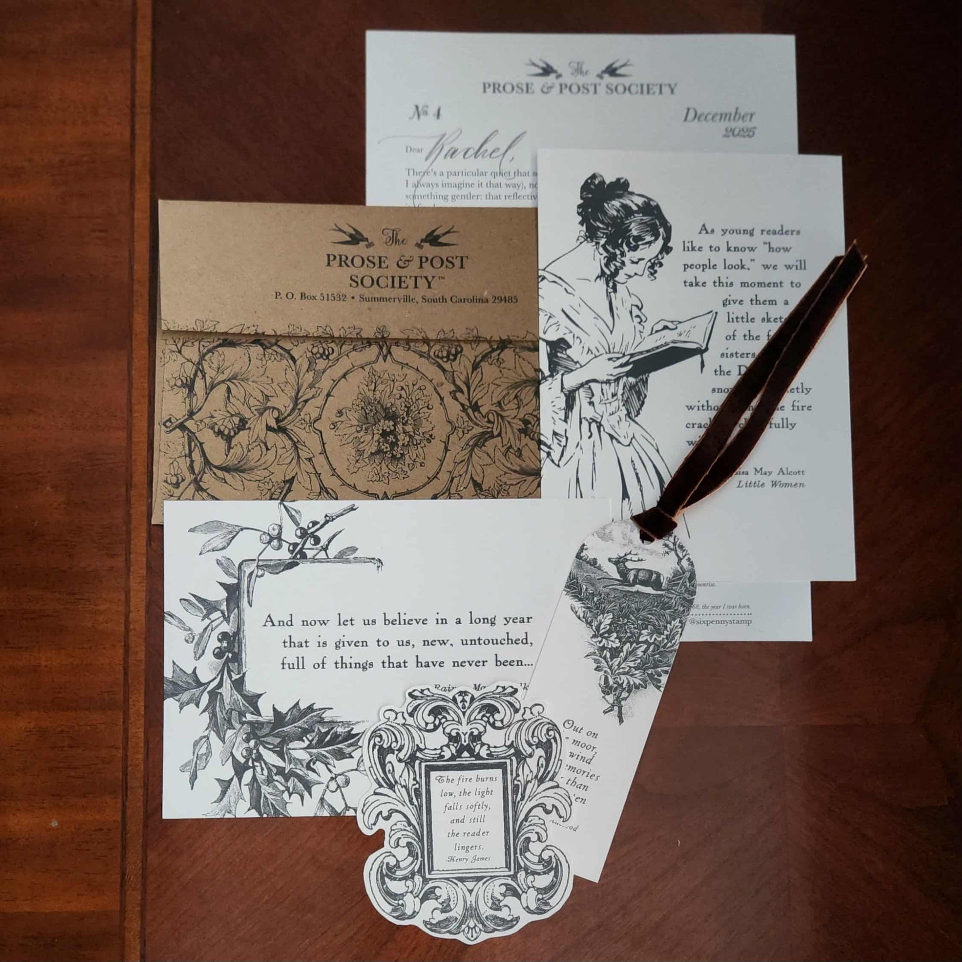 Art prints, envelope, bookmark, letter, and sticker from The Prose & Post Society, on a wooden background. 